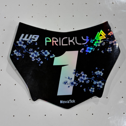 A black motocross number plate with blue floral graphics and a holographic rainbow '1' on a white pegboard background.