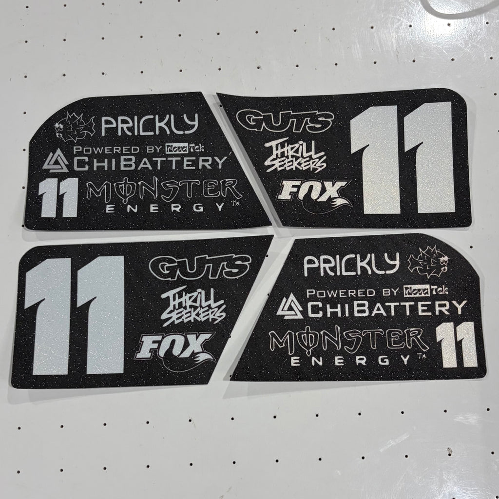 Four black foam decals with white and silver graphics for a racing livery, featuring the number 11 and sponsor logos like Prickly, ChiBattery, Guts, Thrill Seekers, and Fox, arranged on a white pegboard background.