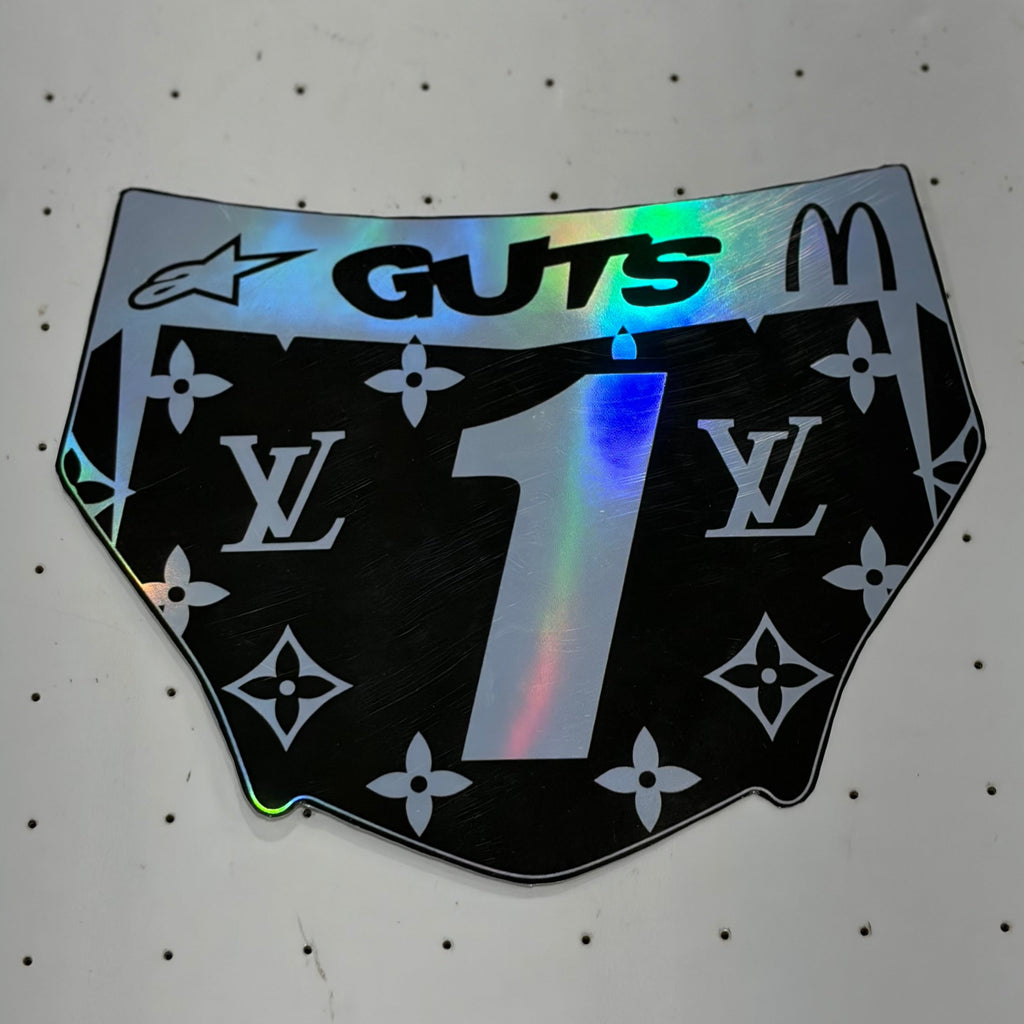 A novelty sticker shaped like a pair of underwear, featuring a black background with the Louis Vuitton monogram pattern, a large holographic number '1' in the center, 'GUTS' in black text at the top, and a McDonald's arches logo on the right side.