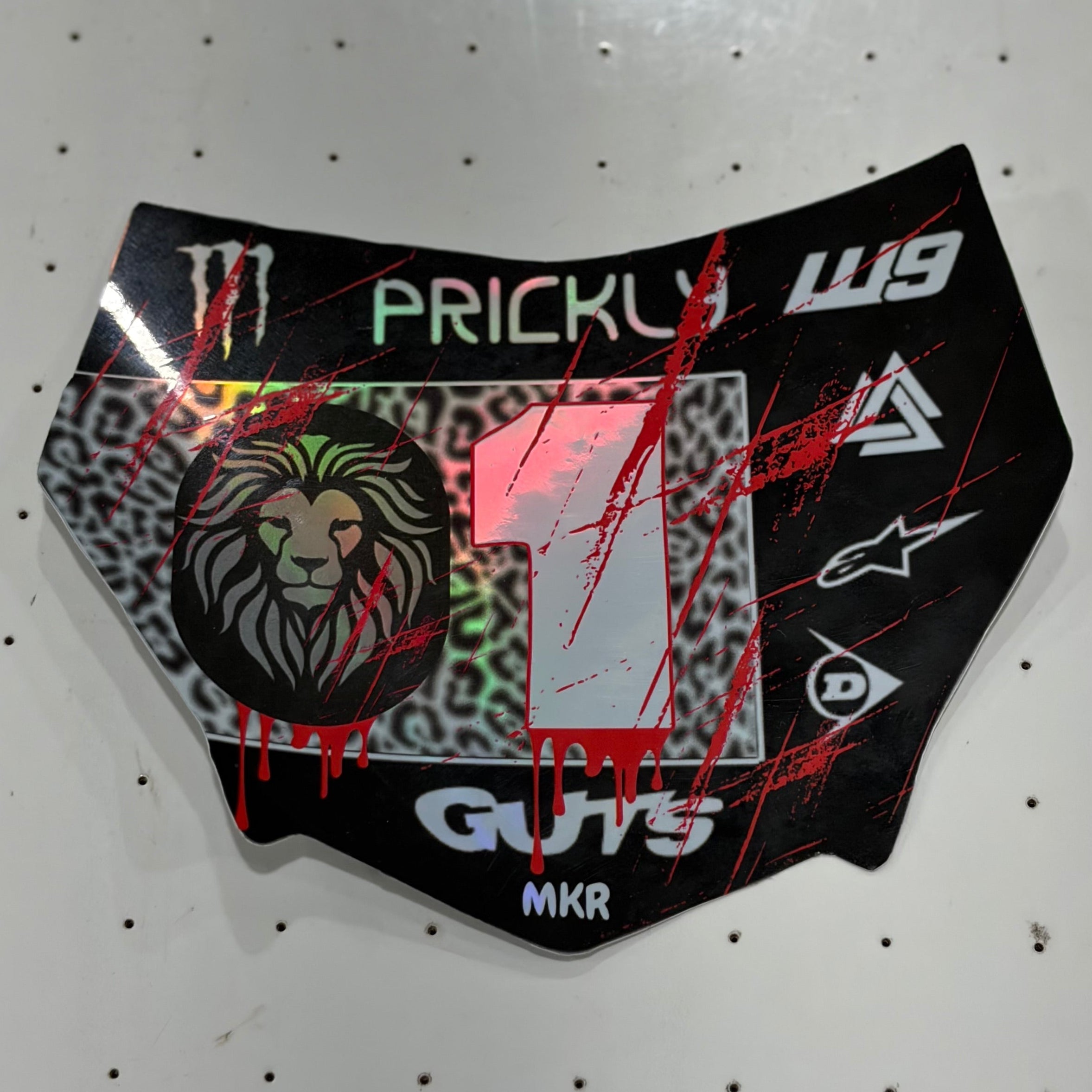 A custom motocross or dirt bike number plate skin decal, featuring a black base with red paint splatters, a green and black leopard print background, a lion graphic, and white text including 'PRICKLY' and 'W9'.