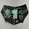 A black protective decal or skin piece for a motorcycle tank, featuring a split design with a green-tinted holographic number 1 in the center, a Fox Racing head logo, a Monster Energy claw logo, and a black scale pattern on one side and a white fox head logo on the other.