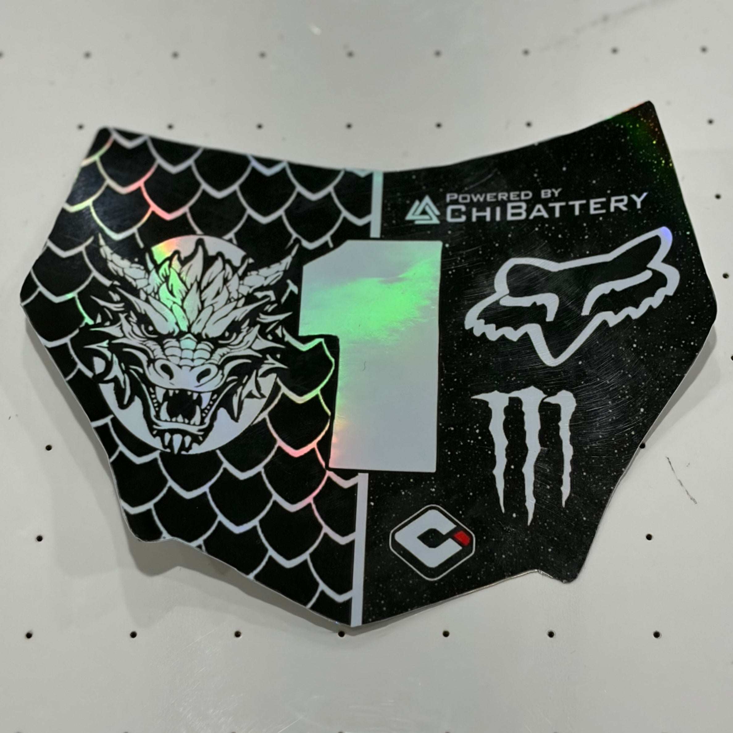 A black protective decal or skin piece for a motorcycle tank, featuring a split design with a green-tinted holographic number 1 in the center, a Fox Racing head logo, a Monster Energy claw logo, and a black scale pattern on one side and a white fox head logo on the other.
