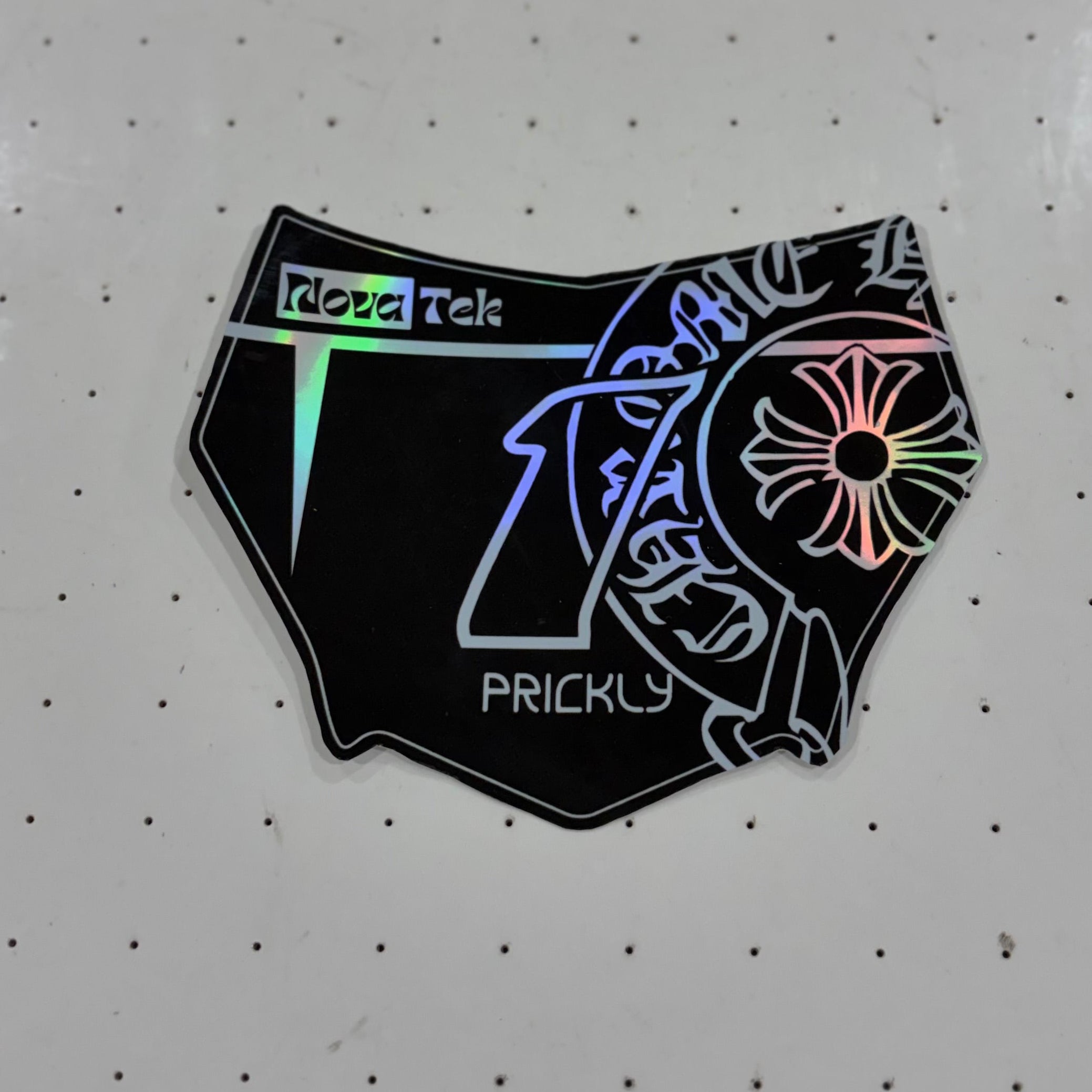A black enamel lapel pin shaped like underwear, featuring a stylized tiger design and a neon rainbow holographic effect, placed on a white perforated surface.