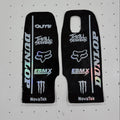 Two black motocross stickers with various sponsor decals, including Dunlop, Fox Racing, EBM X, Monster Energy, and NovaTek, displayed on a white pegboard background.