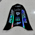 A black motorcycle or electric dirt bike decal sticker set featuring Dunlop branding, Alpinestars logos, and holographic rainbow accents, displayed on a white pegboard surface.