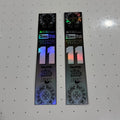 Two long rectangular black stickers with holographic rainbow reflections and printed graphics, including the number 11 and Fox Racing branding, placed on a white pegboard surface.