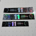 Three rectangular black stickers with holographic and multicolor printed graphics, laid horizontally on a white pegboard background. The stickers feature the text 'GUTS', 'Chibattery', 'Royal Tek Monster Energy', and a large number '11'.